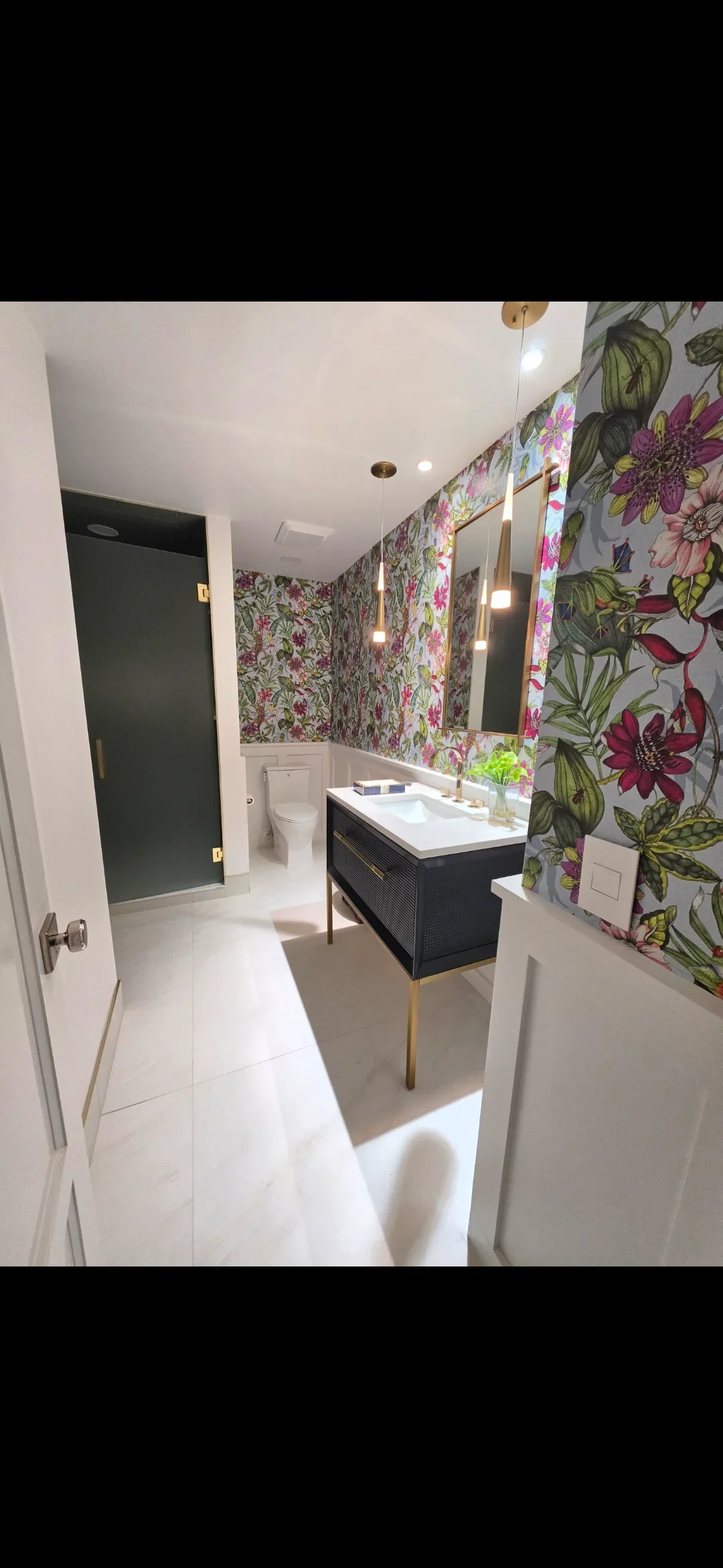 Bathroom with floral wallpaper, black vanity, brass fixtures, and white tile flooring
