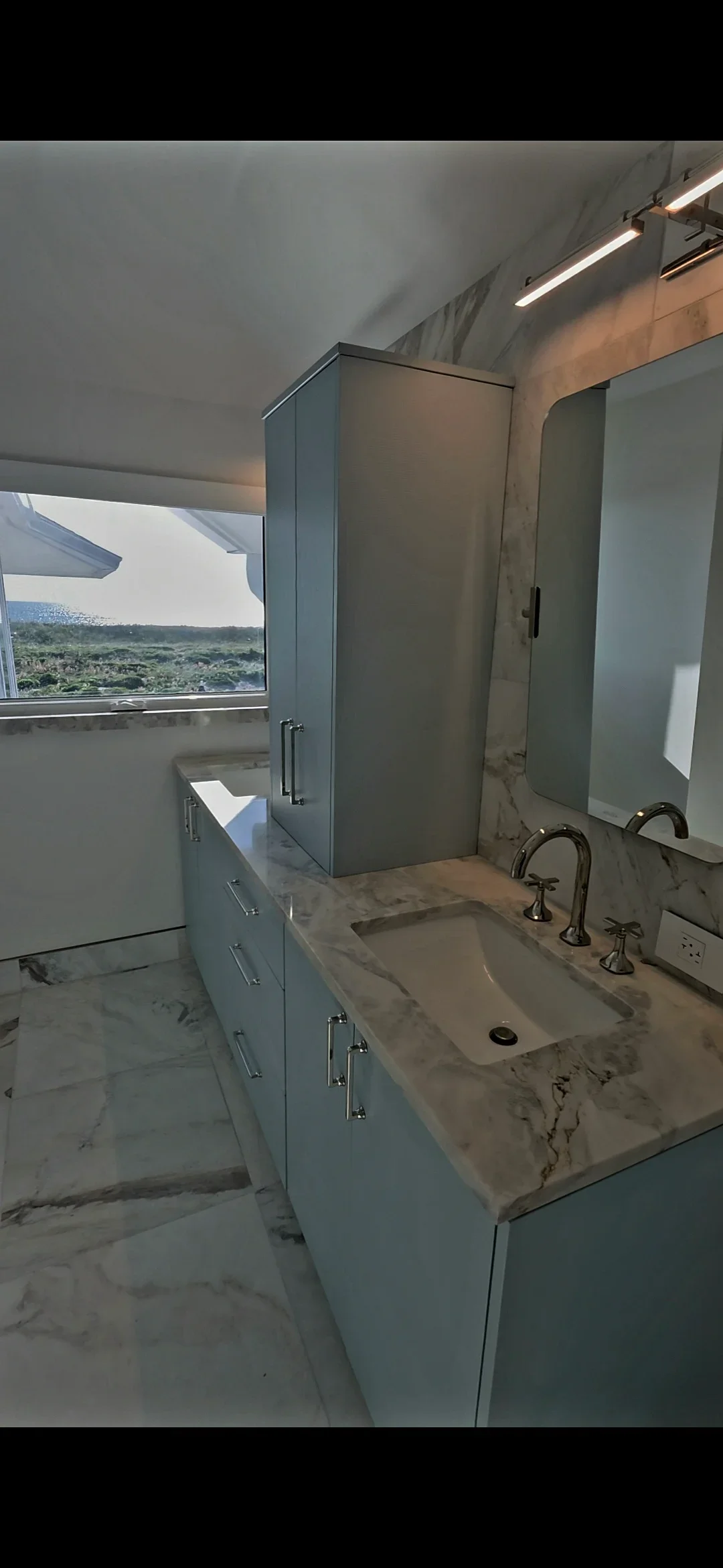 Modern bathroom with marble vanity, dual sinks, glass shower, and floating cabinetry