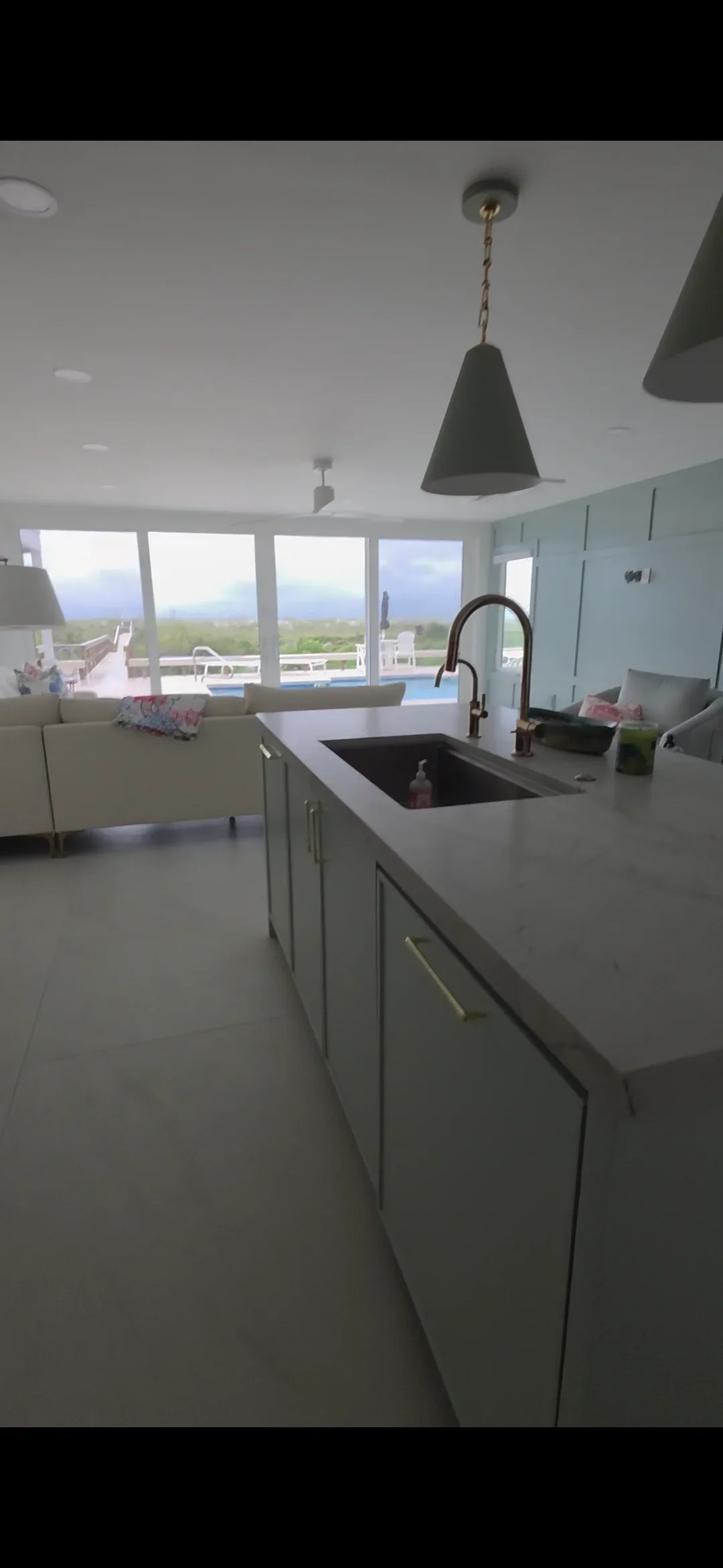 Modern kitchen with sage green cabinetry, quartz counters, island sink, and waterfront windows
